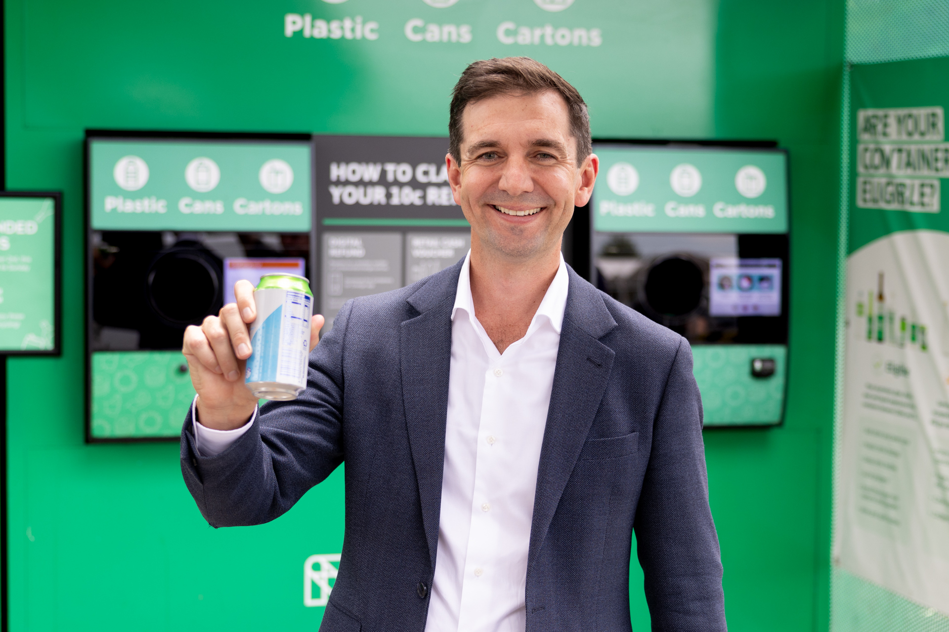 COEX CEO Trevor Evans holding an eligible drink container in front of a Containers for Change reverse vending machine.