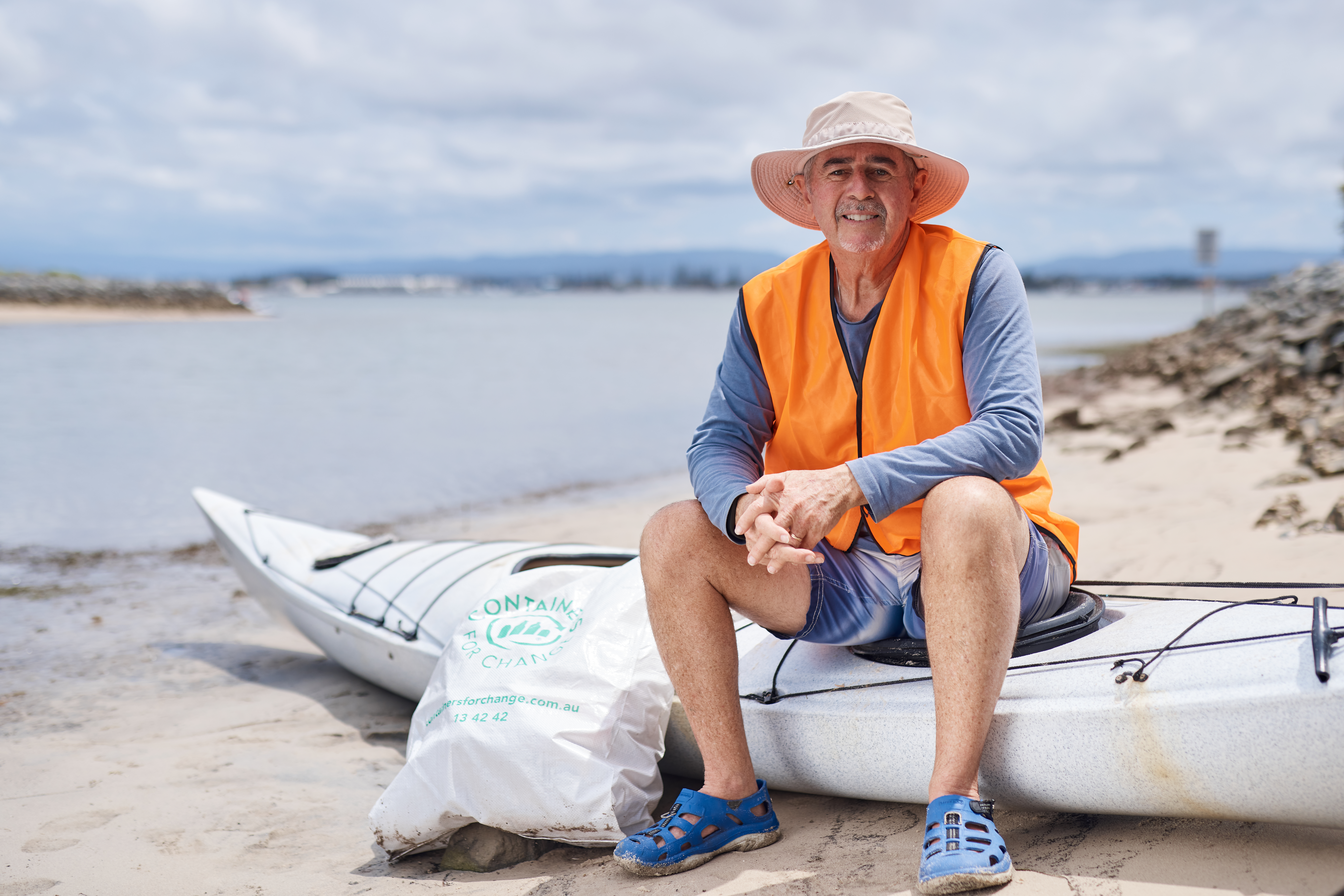 David Sear sitting beside a kayak on a beach with a bag of collected rubbish.
