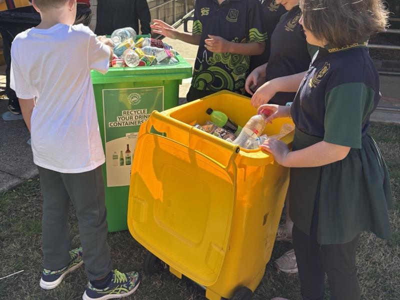 Drayton State School students placing empty drink containers into yellow and green recycling bins.